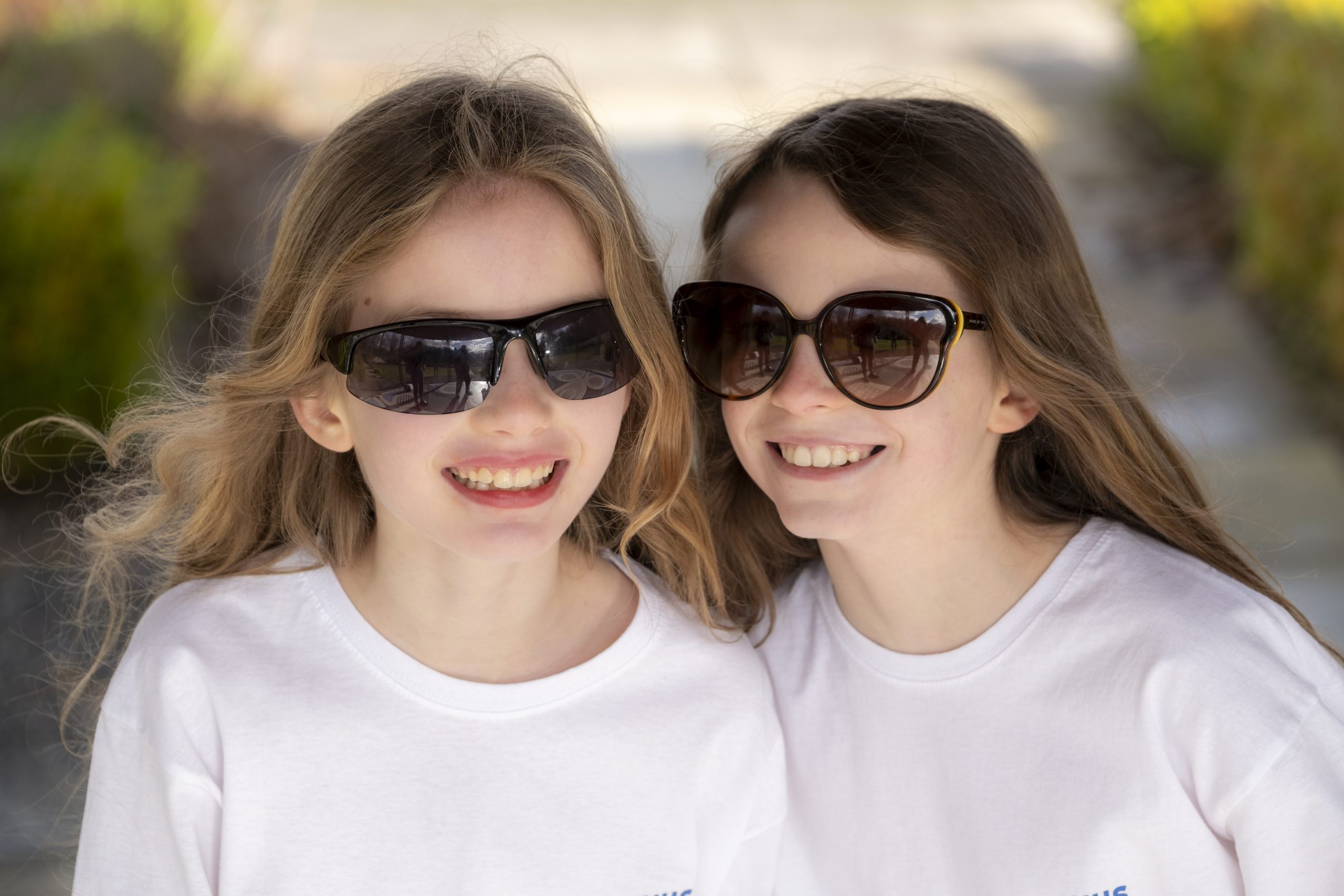 Two young girls wearing big sunglasses and white t-shirts smiling.